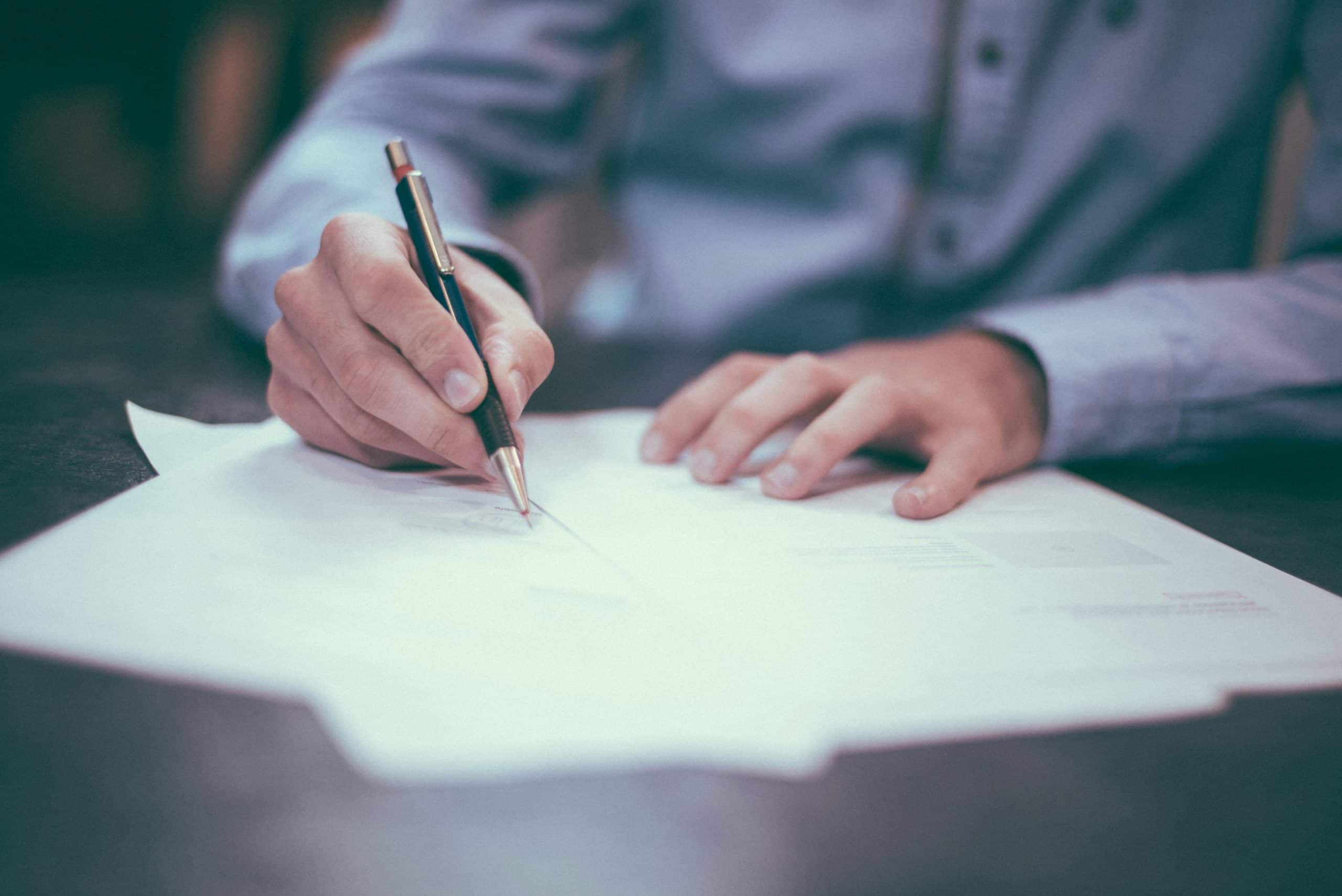 Person signing estate planning documents with pen at desk