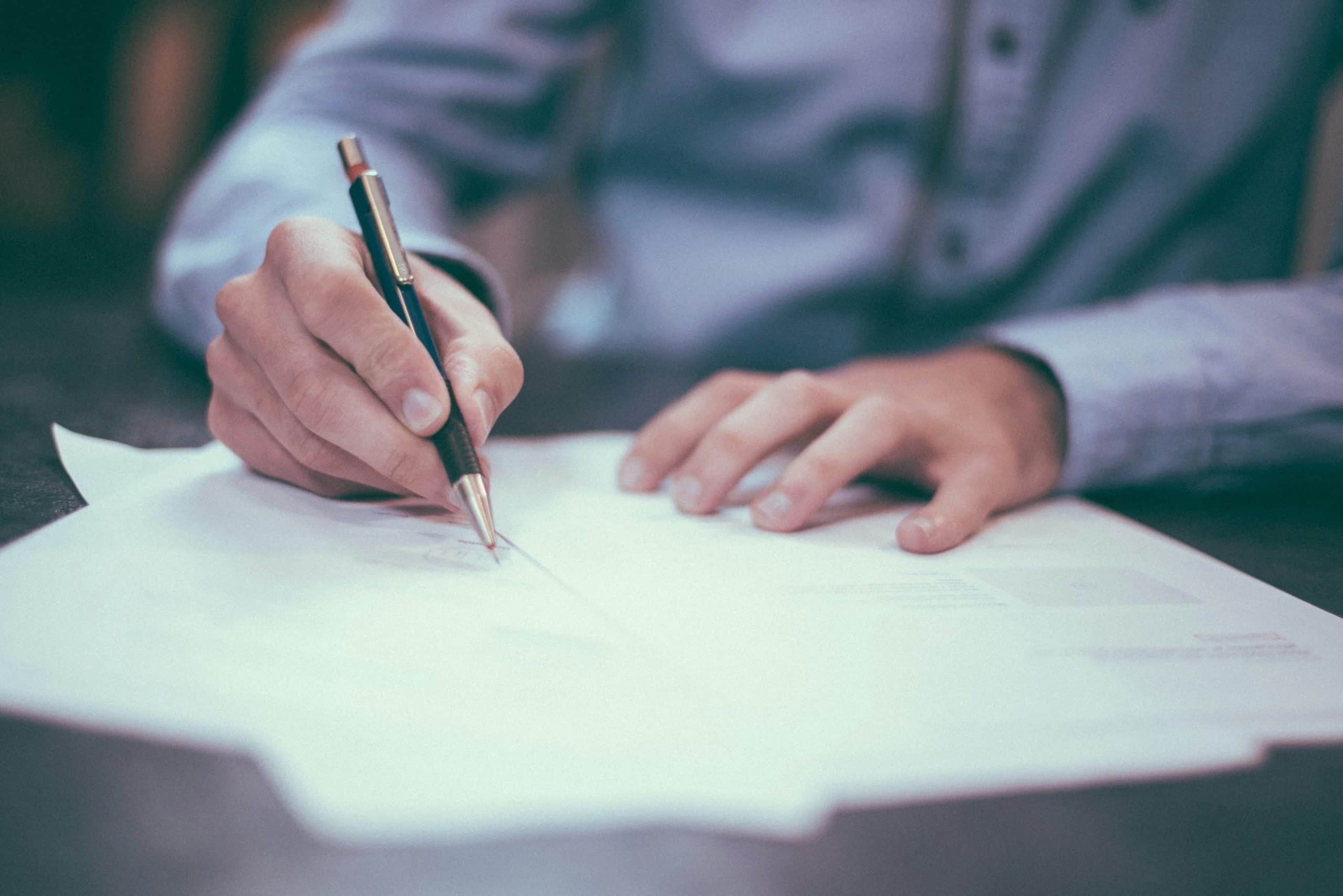 Person signing estate planning documents with pen at desk